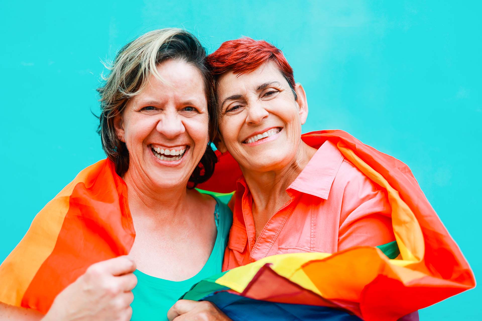 Happy Senior gay lesbian couple having fun wearing Lgbtq rainbow flag at pride parade - Family and love concept - Focus on right woman face